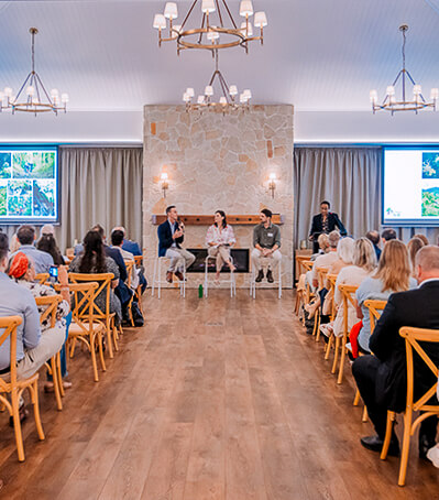 Large group attending a presentation or conference in a light-filled room with a stone fireplace.