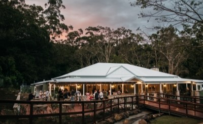 Spacious event venue with veranda, surrounded by trees, at sunset.