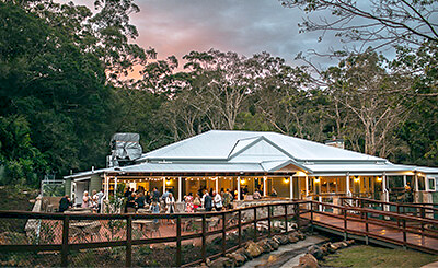 Spacious event venue with veranda, surrounded by trees, at sunset.
