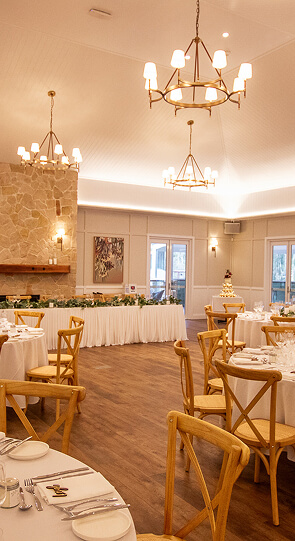 Elegant banquet hall set for a wedding reception with round tables, wooden chairs, and chandeliers.