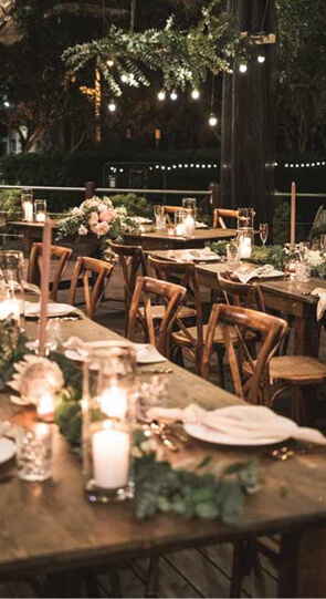 Outdoor evening dinner on The Village Deck with long wooden tables set with candles, greenery centerpieces and string lights