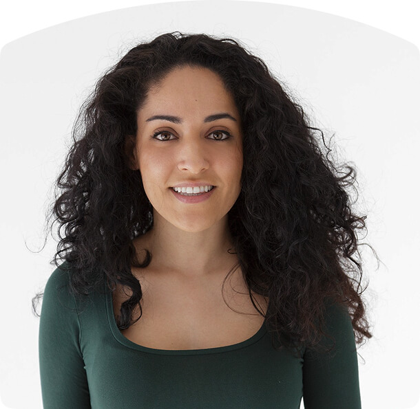 Person with long, curly dark hair wearing a dark green top, smiling slightly while facing forward.