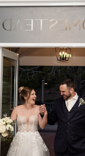 Bride and groom smiling and holding hands as they exit a building