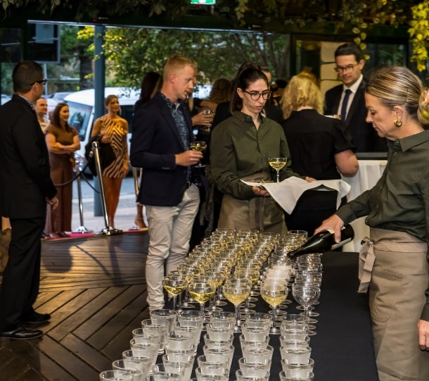 Guests mingling at a corporate event, with a table of champagne glasses being attended by staff in a lively atmosphere.