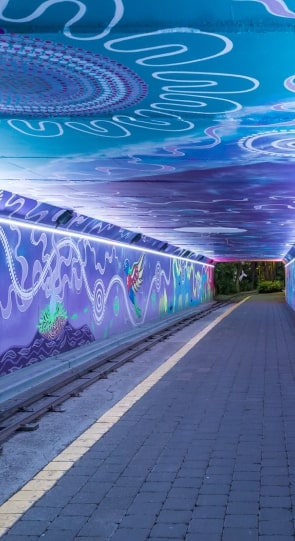 Vibrantly decorated tunnel with purple and blue walls featuring abstract patterns and artwork, leading to a lighted exit.
