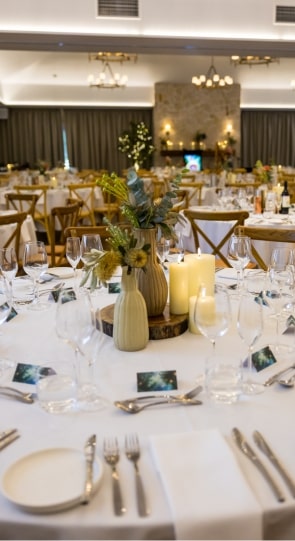 Dining table set for a corporate event, featuring elegant tableware, floral centerpieces, and candles, in a well-lit venue.