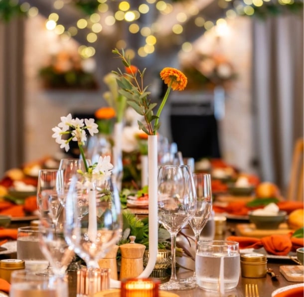 A beautifully arranged dining table with glasses, candles, and flowers, set for a social event with warm lighting.