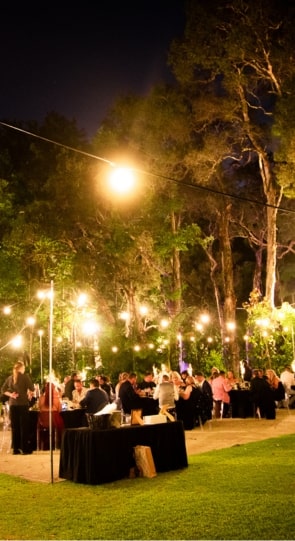 Guests dining at elegantly set tables under string lights in a lush garden during a nighttime wedding reception.