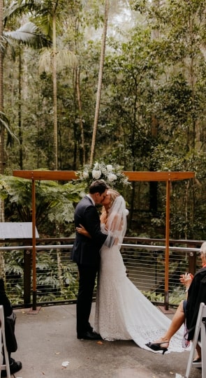 Couple exchanging vows at an outdoor wedding ceremony in a lush forest setting, surrounded by greenery and guests.