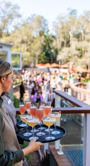 A server holds a tray of colorful cocktails while guests mingle in the background at a wedding reception.