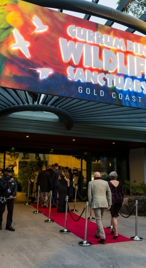 Guests waiting in line on a red carpet in front of the Currumbin Wildlife Sanctuary entrance, with a colorful sign overhead.