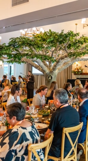Guests enjoying a meal at a social event, with a large decorative tree in the center