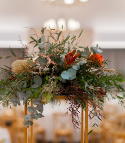 Floral centerpiece with eucalyptus, red flowers, and greenery in a wedding venue setting.