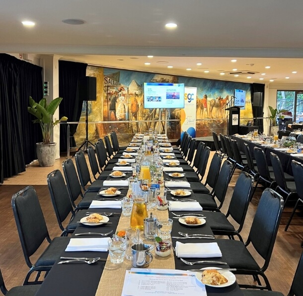 Long banquet tables in the Sawrey Room set for a catered meeting—plates, napkins, glasses and juice pitchers