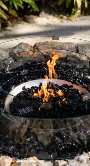 Outdoor electrical fire pit at The Pavilion: orange flames over black fire glass inside a circular glass guard