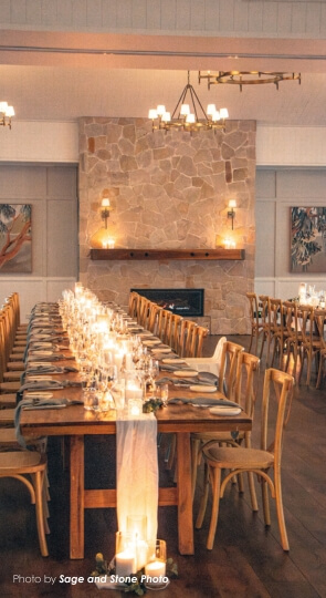 Elegant dining setup with long table, candles, and stone fireplace.