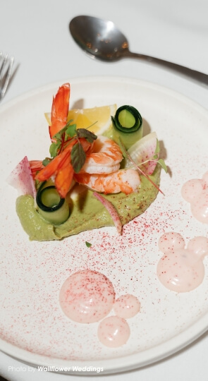 Prawns and cucumber swirls on avocado cream, garnished with microgreens and drops of light pink cream on a white plate