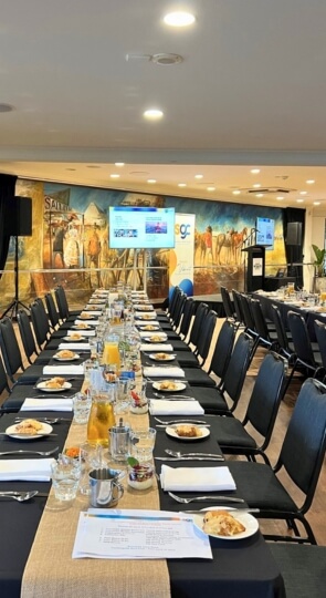 Sawrey Room: long banquet tables set for breakfast with plates, glasses and juice; cowboy mural and presentation screens