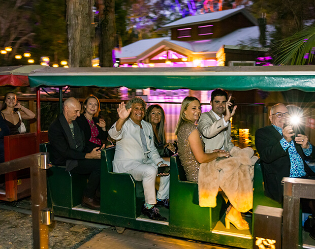 Group of people waving on a decorated train ride at night.