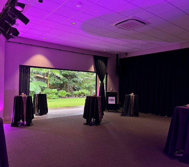 Reception space at Sir Walter Campbell Theatre with purple uplighting, draped cocktail tables and wide open doors