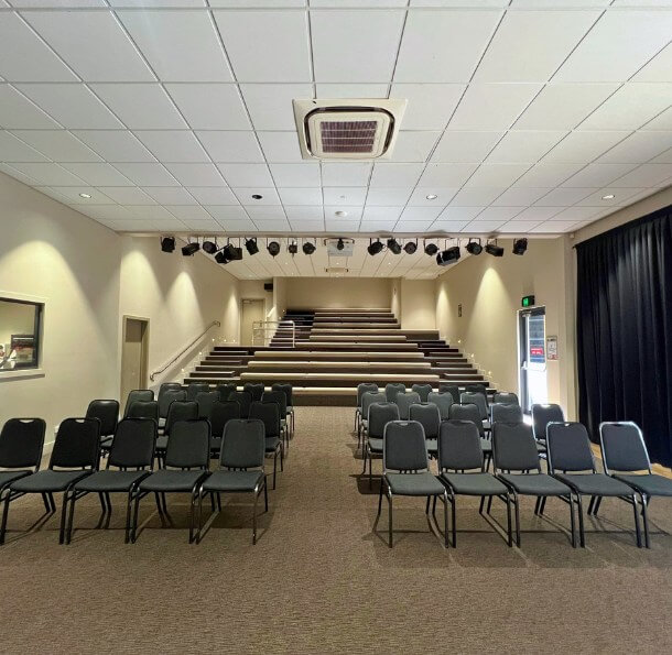 Sir Walter Campbell Theatre auditorium with black chairs arranged in rows facing tiered seating and overhead stage lights