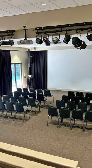 Sir Walter Campbell Theatre interior with rows of black chairs facing a projection screen, stage lighting overhead