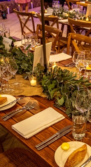 Close-up of Sawrey Room table set with eucalyptus garland, lit votive candles, wine glasses, folded napkins and bread plates.