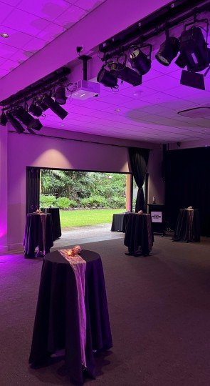 Sir Walter Campbell Theatre reception lit purple with cocktail tables draped black, doors open to a green garden