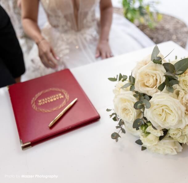 Wedding white rose bouquet beside a red signing book with a gold pen on a white table