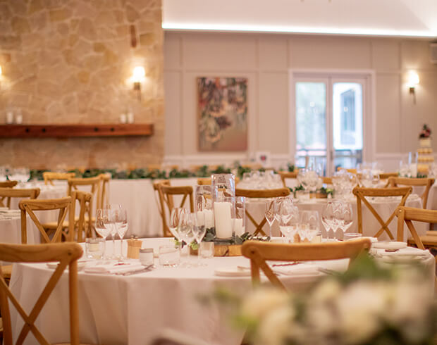 Elegant wedding reception setup with wooden chairs and white tablecloths.