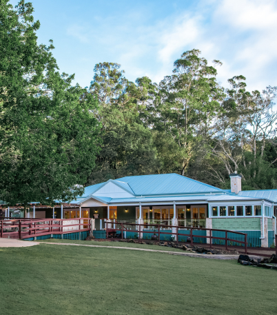 A beautiful Queensland inspired homestead with a large outdoor wrap around verandah, set in the middle of large green trees and lush green grass fields