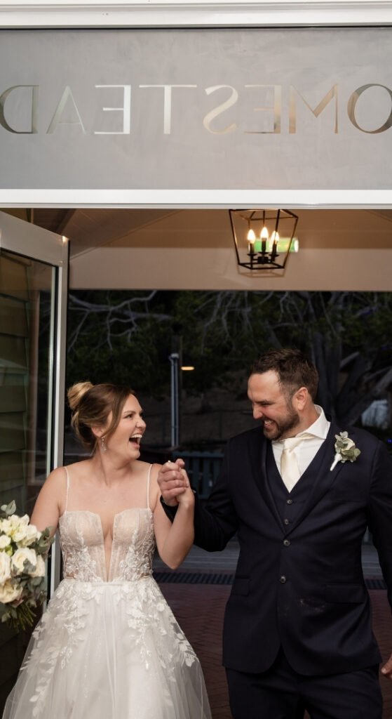 Bride and groom smiling and holding hands as they exit a building