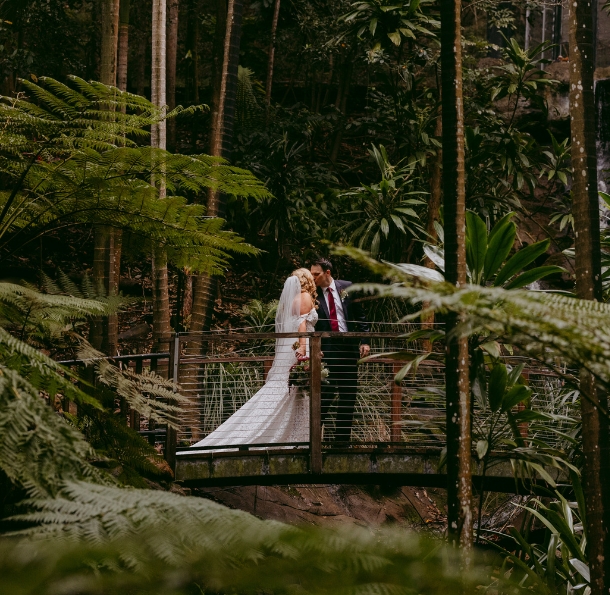 Kissing wedding couple on a wooden bridge in a lush rainforest
