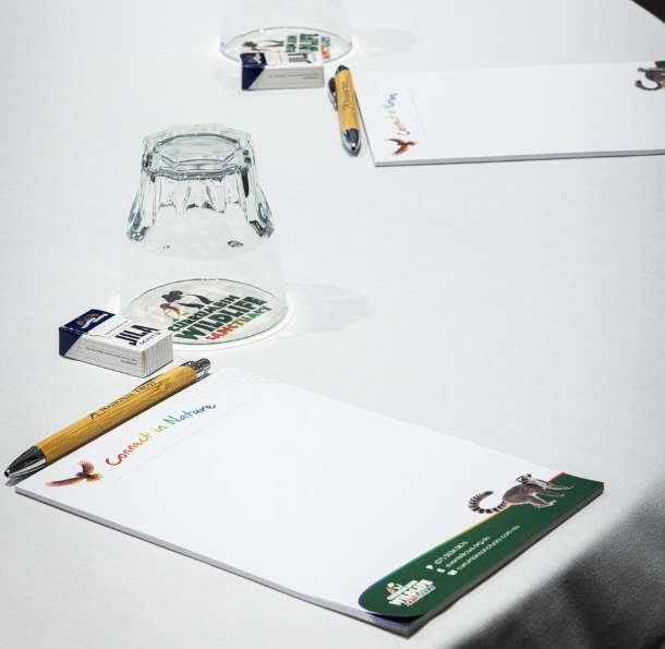 A set of two wildlife branded pads, pens, mints, drink coasters and water glasses on a table nicely set with a white tablecloth.