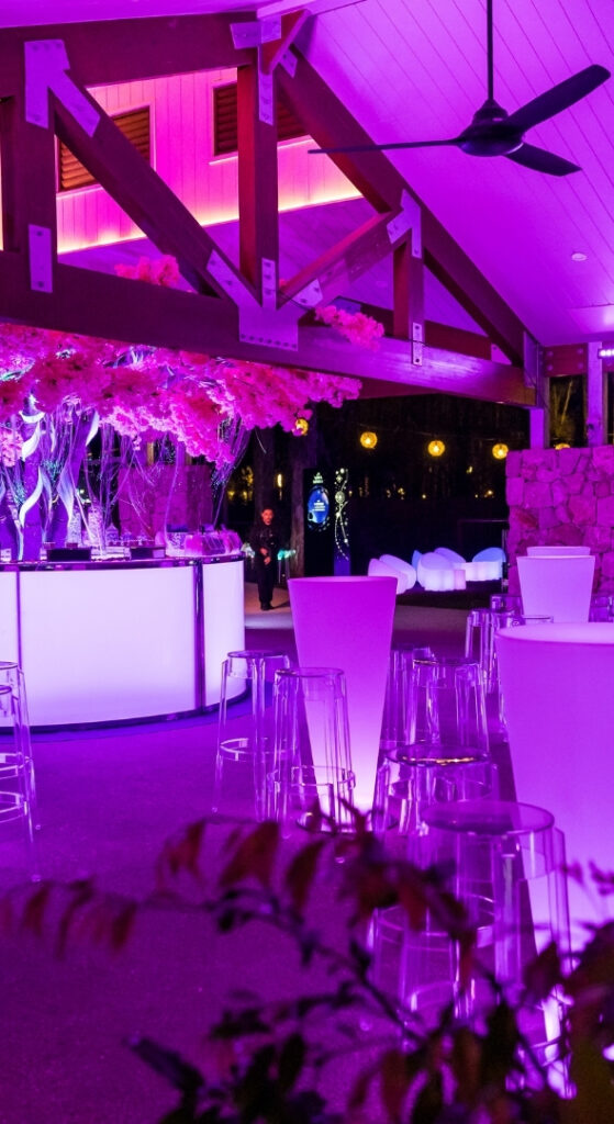 Cocktail bar area under a pavilion with pink floral lighting installation and purple uplighting at night