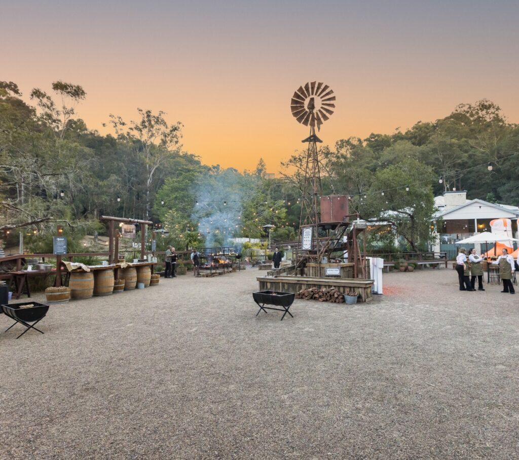 Wide view of the Outback Springs event space at dusk with windmill, fire pits and open gathering area, Currumbin Wildlife Sanctuary