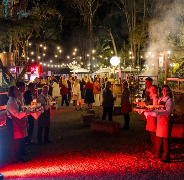 Waitstaff serving canapés to guests at a night event at Outback Springs, Currumbin Wildlife Sanctuary. The outdoor space is lit with red light projections and festoon lights
