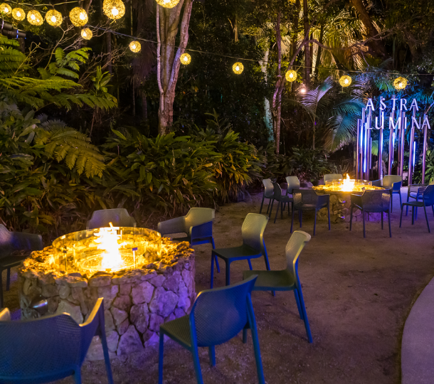Outdoor seating area with stone fire pits and festoon lighting near the Astra Lumina sign at night