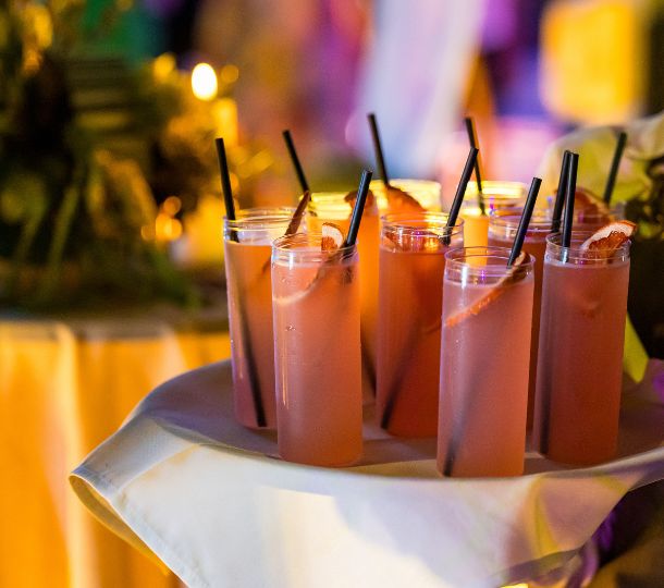 A tray laid with a white cloth holding ten pink cocktails each with a slice of dried orange